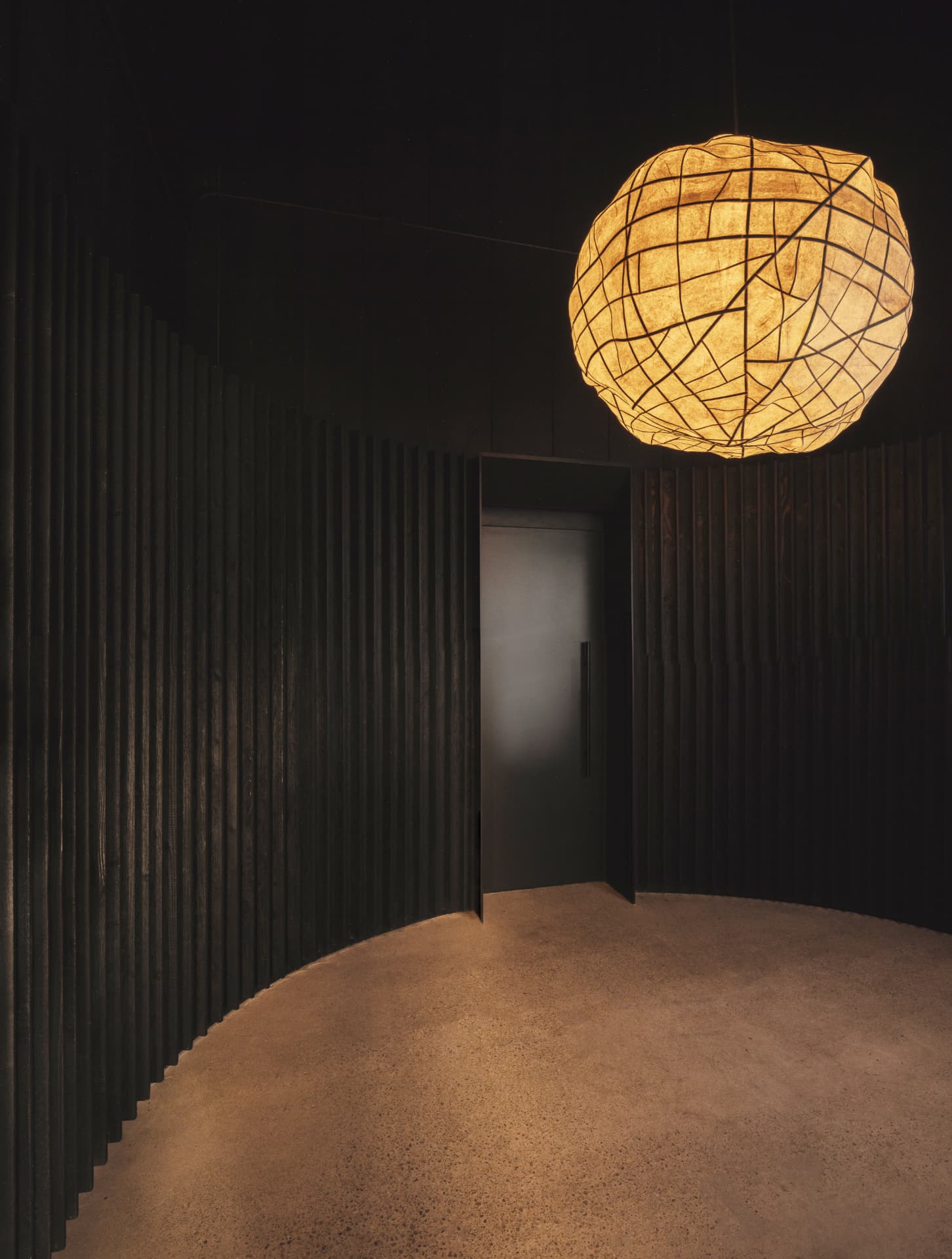 Woven paper pendant glowing above a dark slatted vestibule
