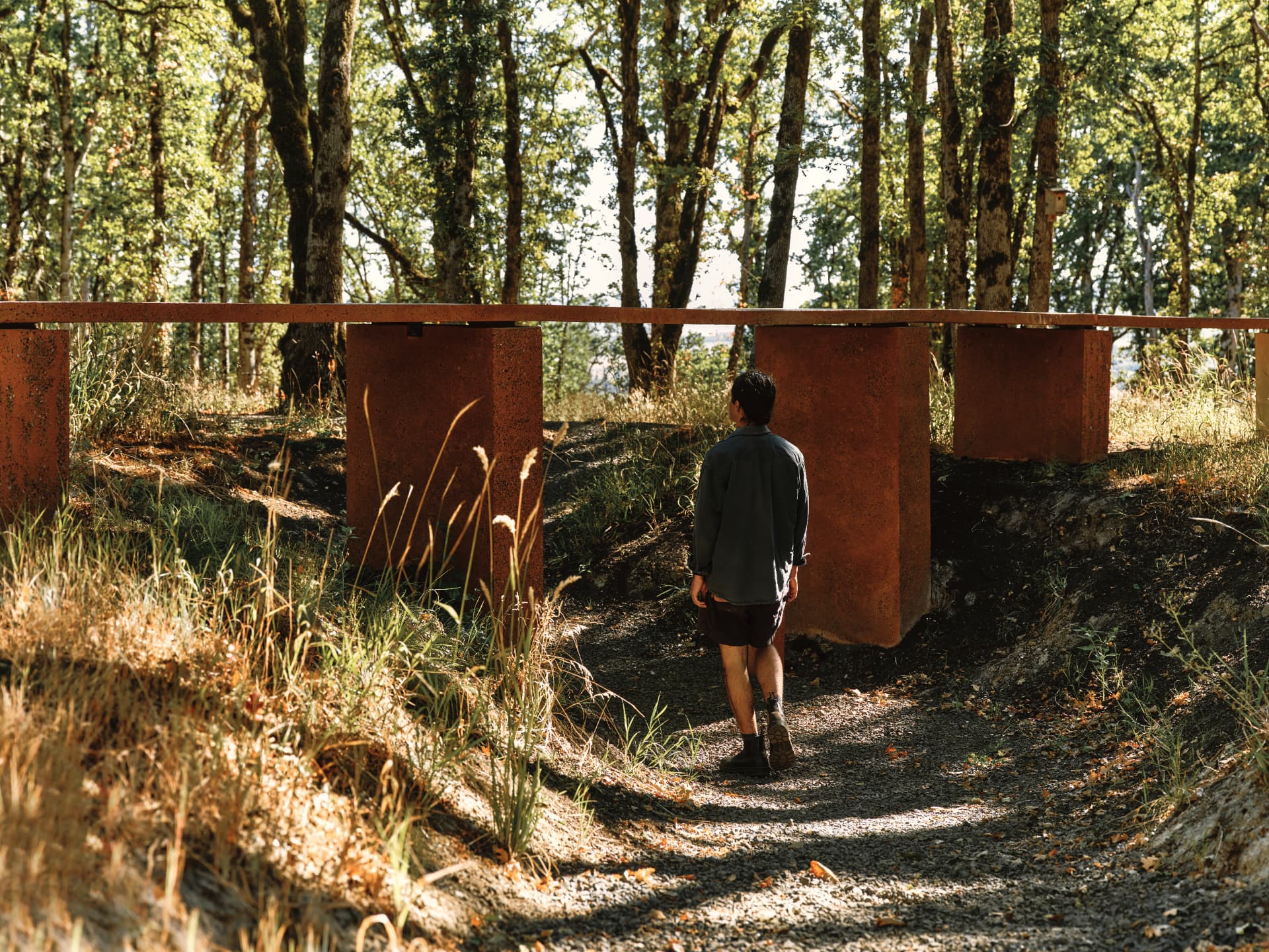 A visitor walking the gravel path beneath the table's terrazzo plinths