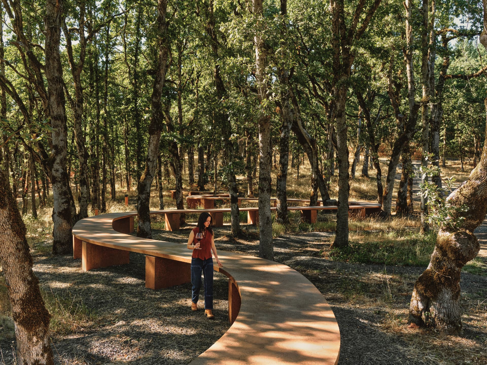 A visitor walking beside the S-curve of the terrazzo table in dappled light