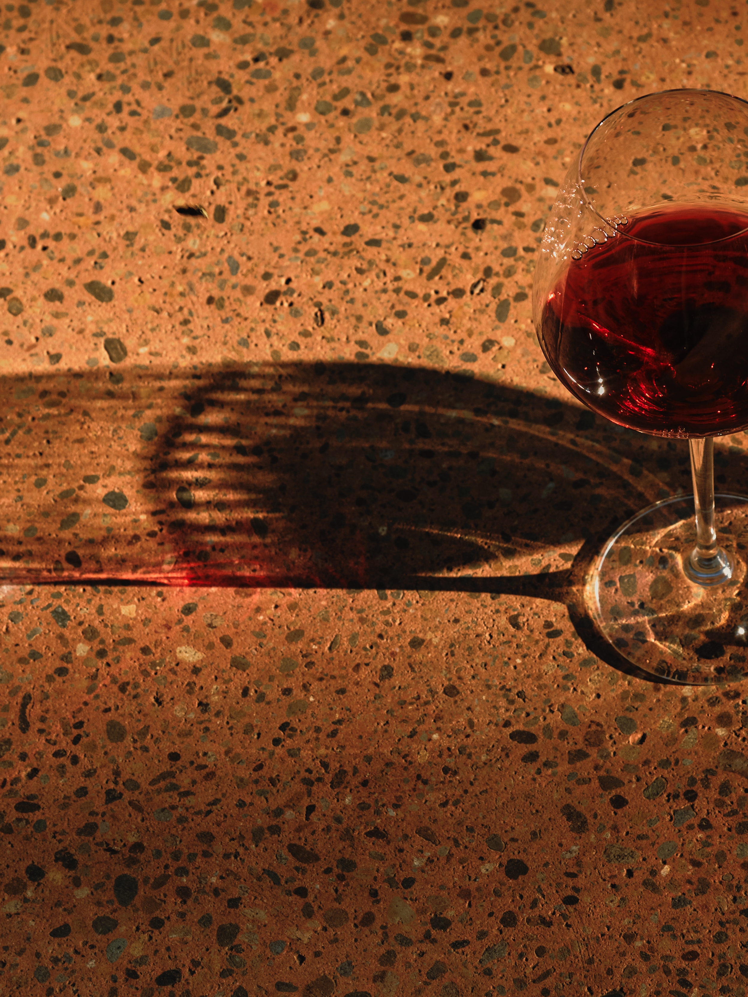 Glass of red wine on terracotta terrazzo with a long shadow
