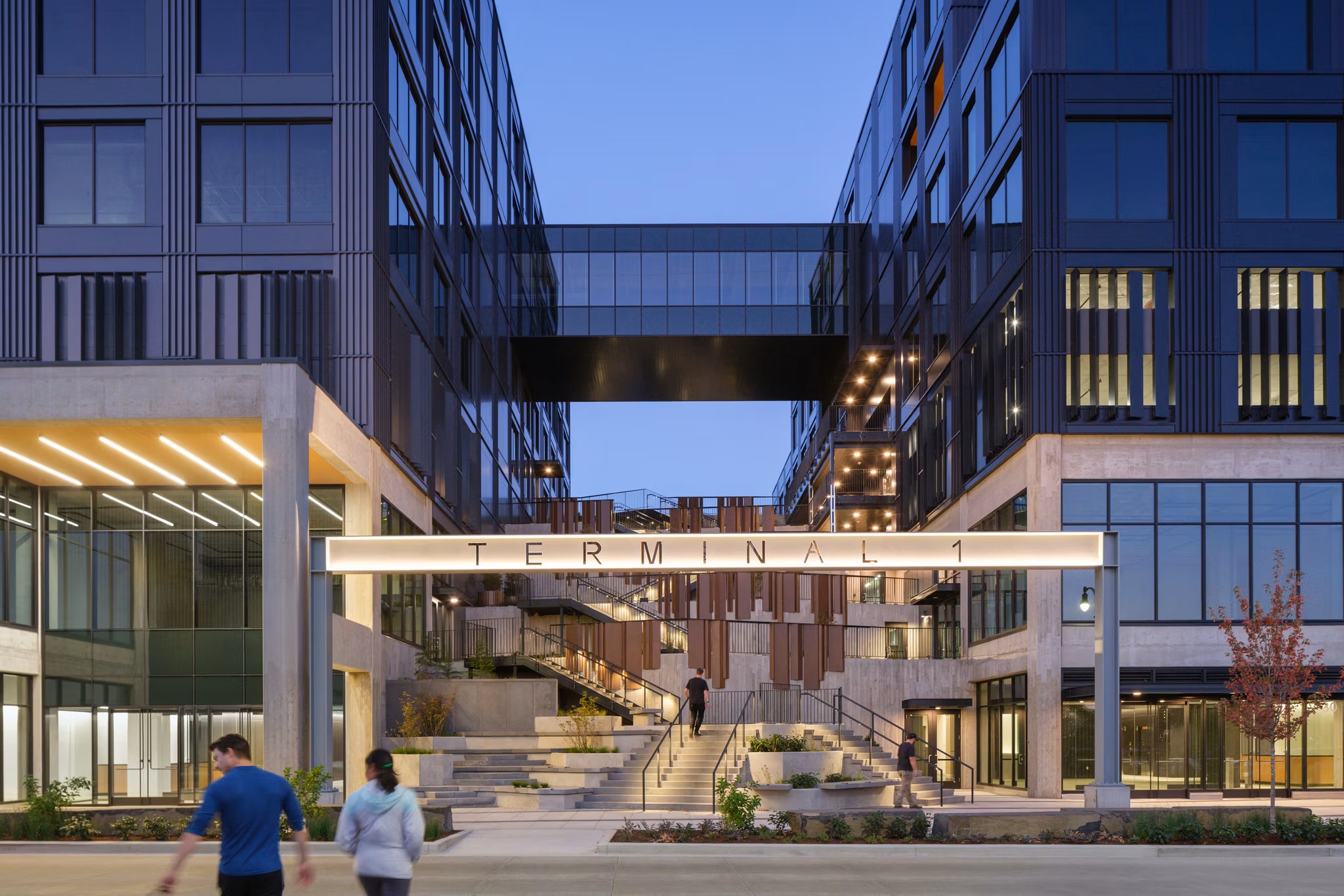 Illuminated TERMINAL 1 sign spanning the courtyard stair at blue hour