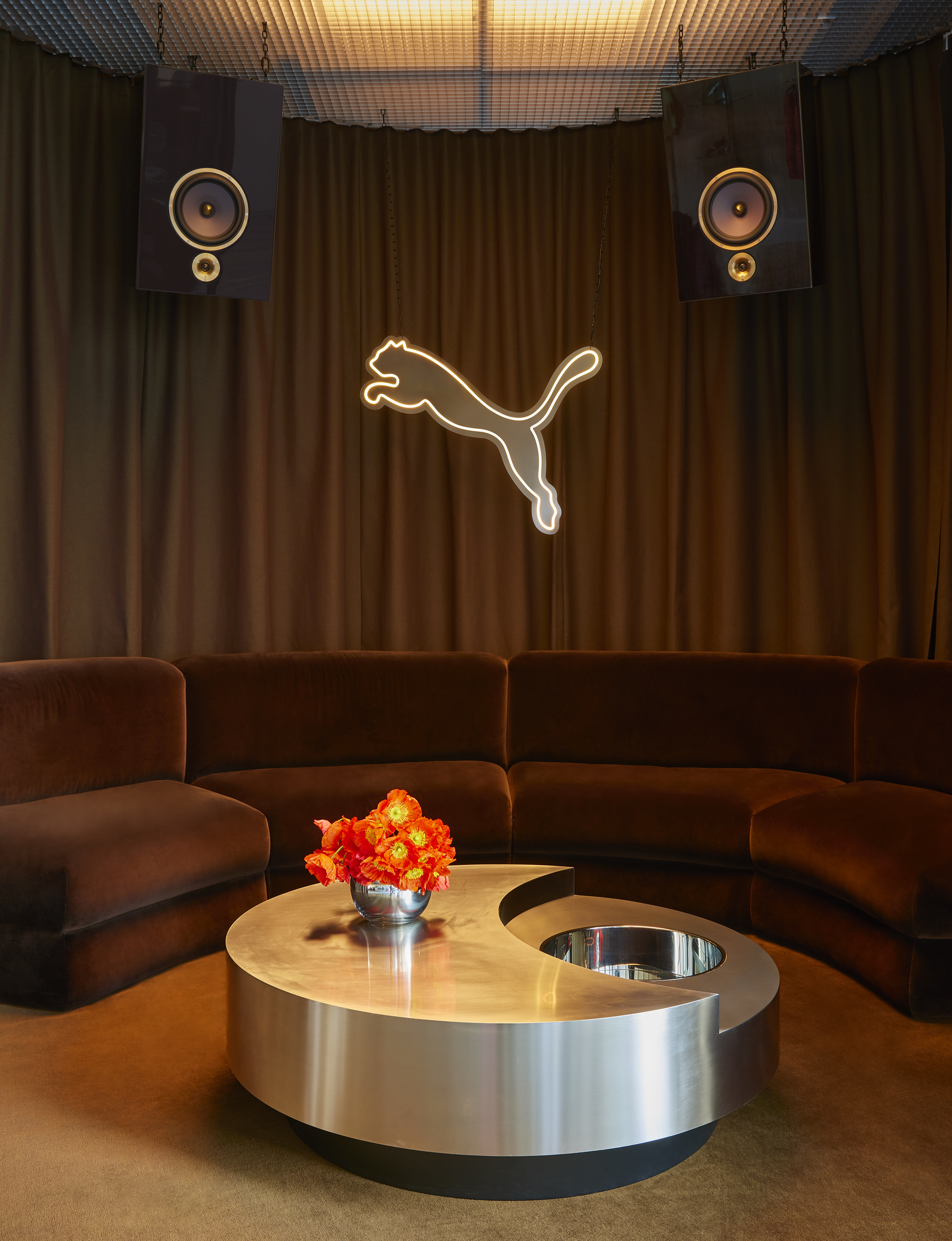 Curved brown velvet banquette beneath a neon Puma cat and suspended speakers