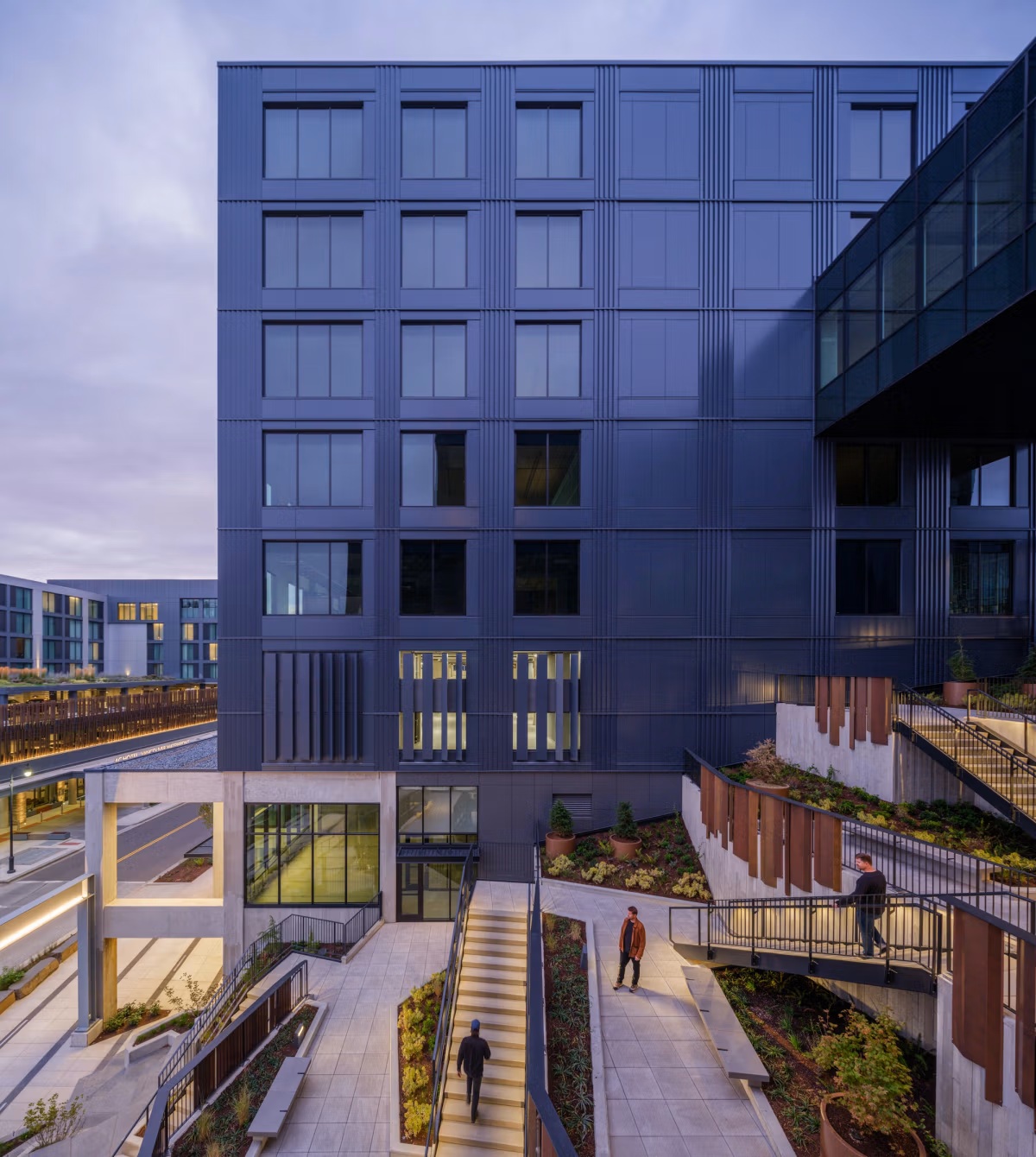 Terraced courtyard stairs, planters and weathering-steel screens below the office volumes