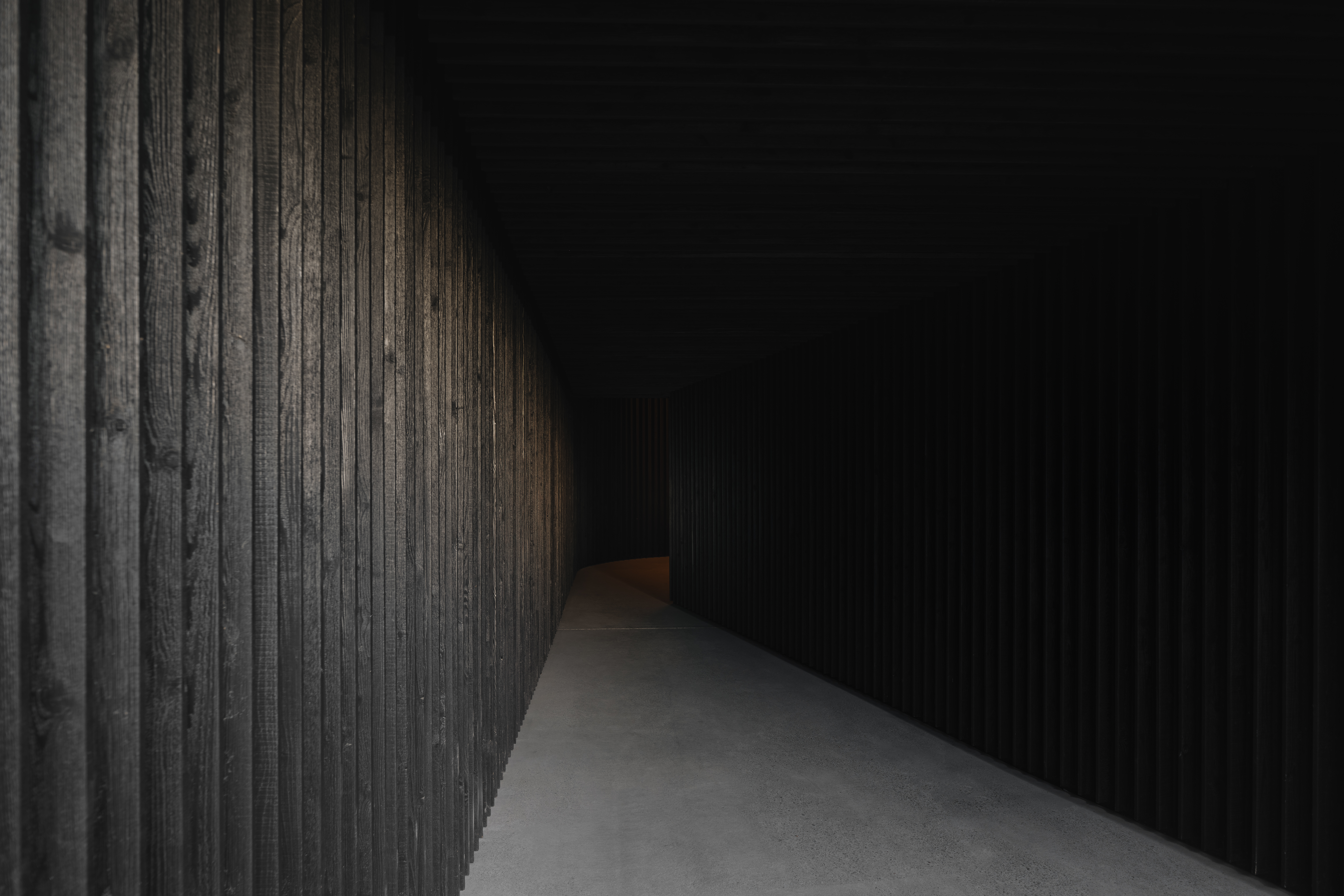 Charred timber corridor leading toward a warm glow