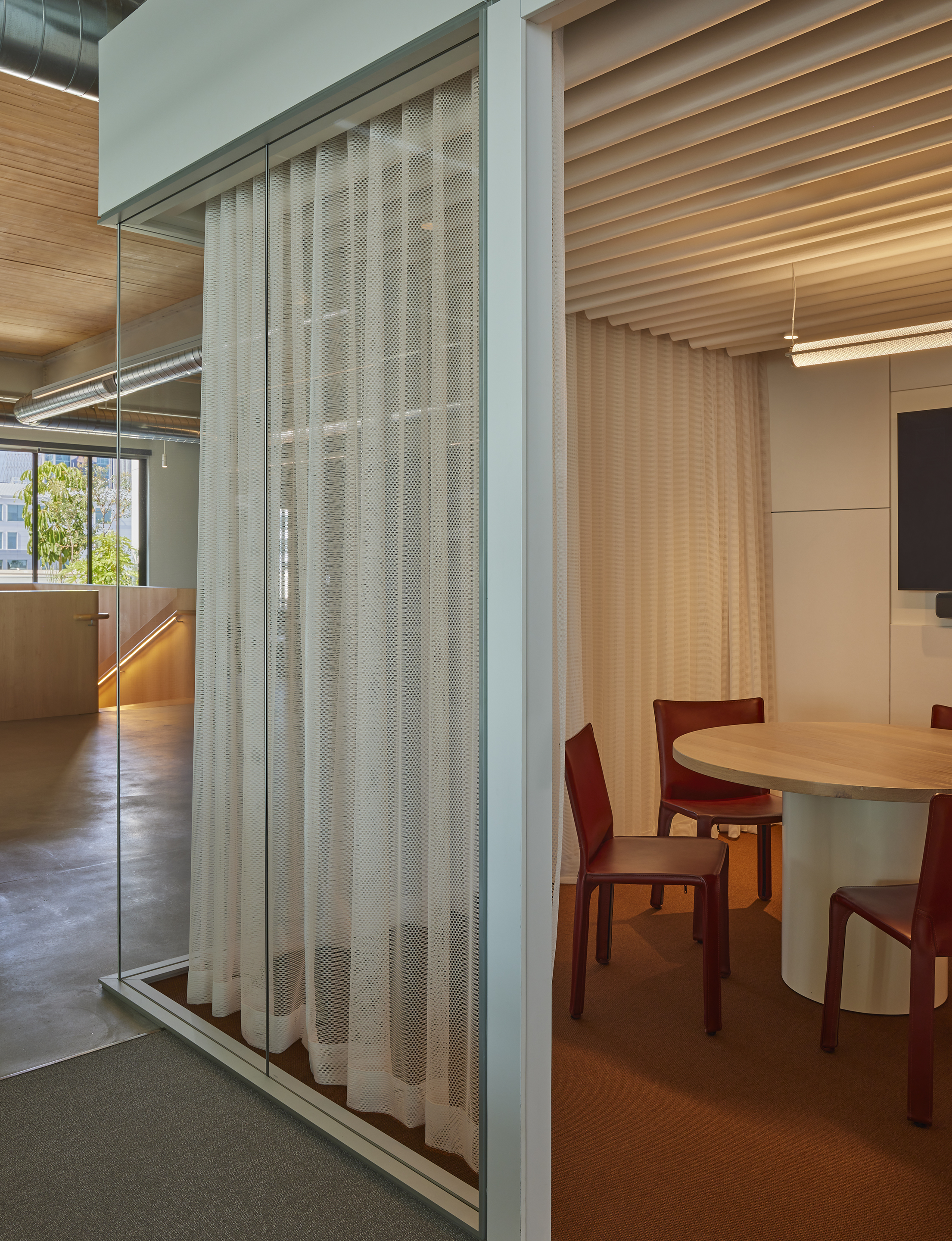 Mesh curtain behind a glass partition beside a meeting room with red leather chairs