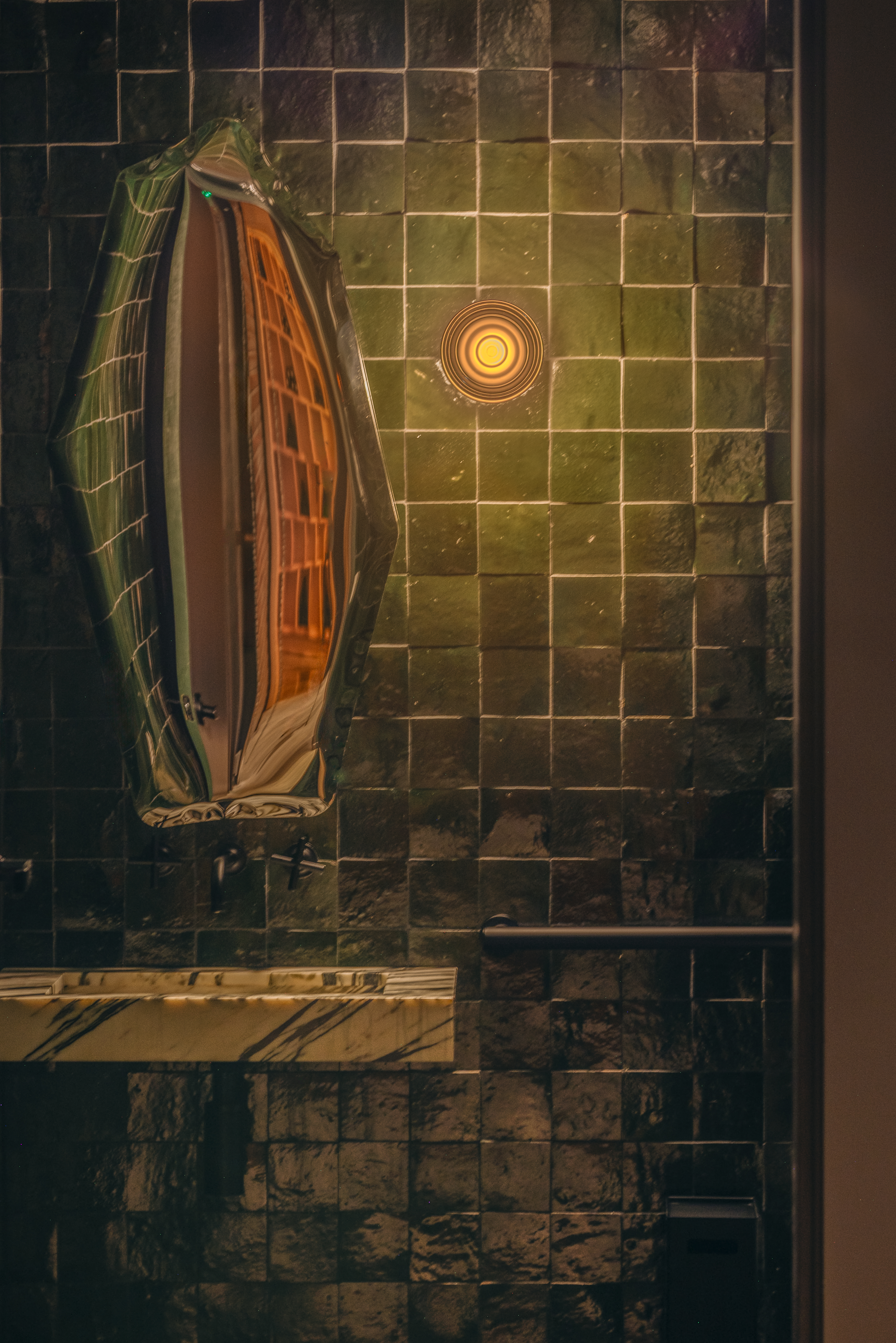 Green-tiled washroom with sculptural mirror and marble sink edge
