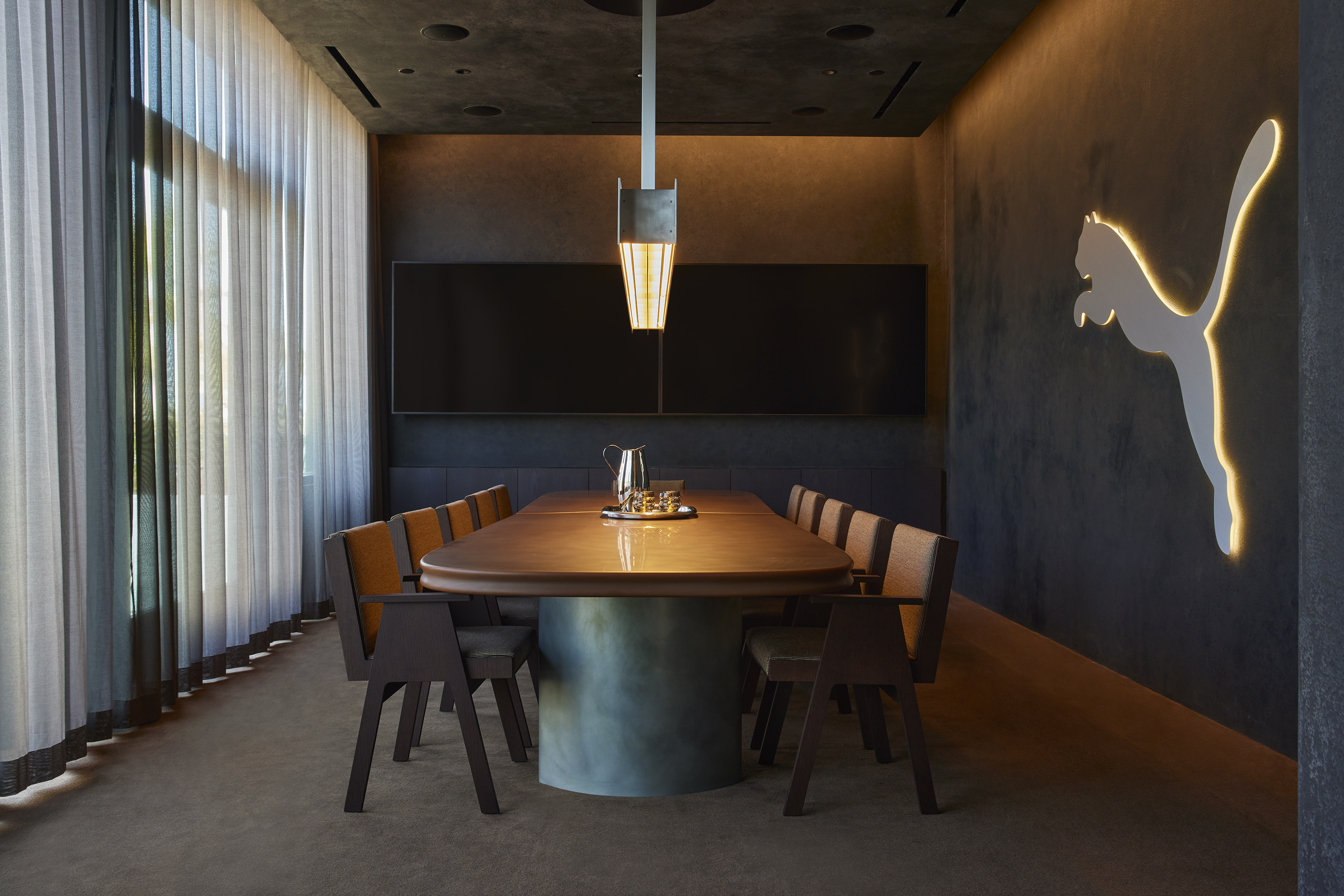Boardroom with an oval table, sheer curtains and an illuminated Puma cat on the wall