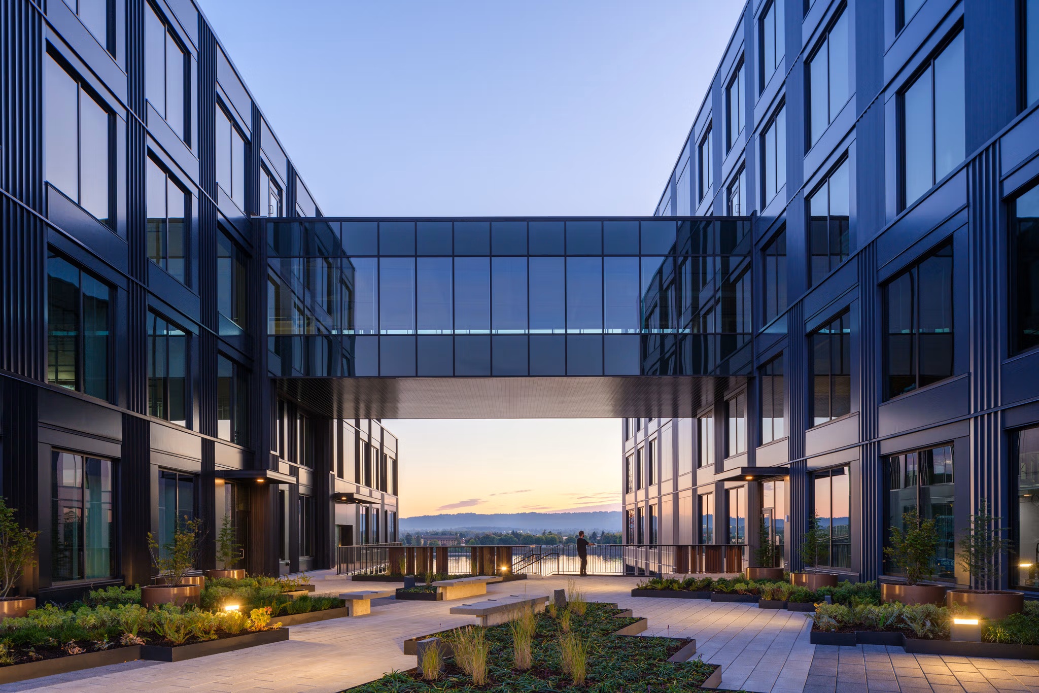 Glazed skybridge framing a sunset view over the river from the upper courtyard