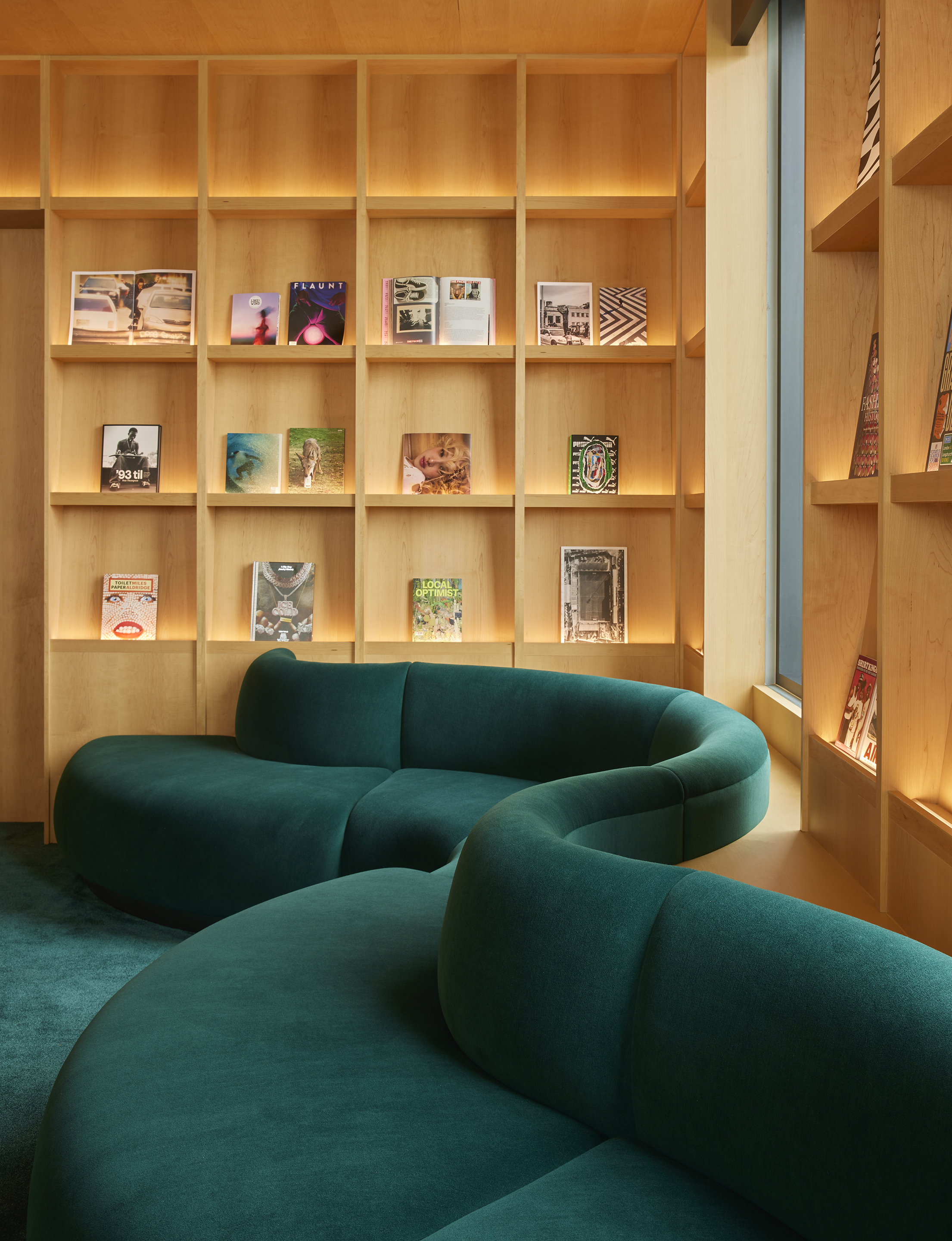 Backlit maple shelving with magazines above curved green seating