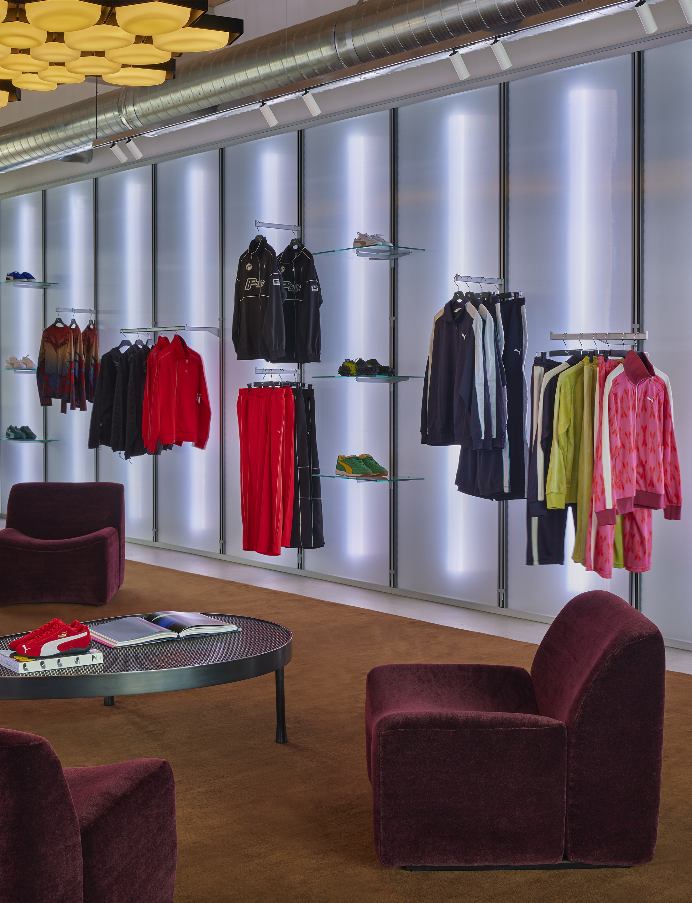 Backlit display wall with garment rails and glass shelves of footwear