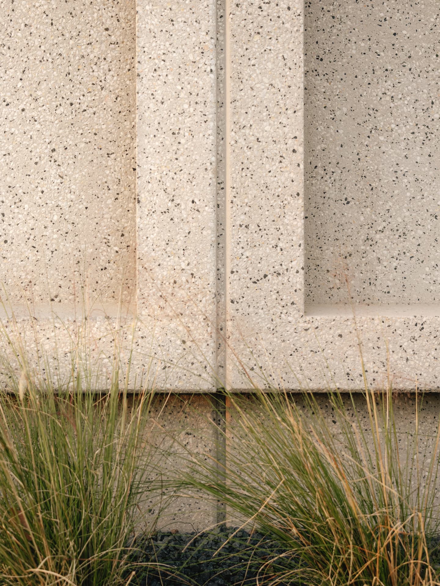 Close detail of textured precast concrete meeting grasses at the facade base
