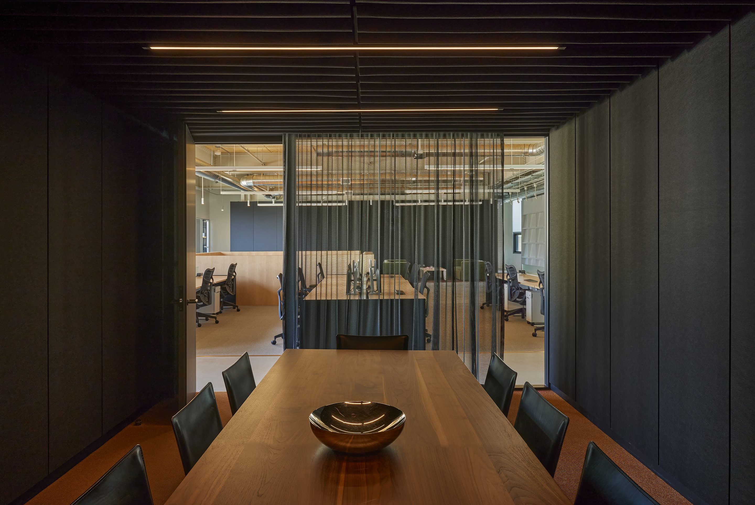 Dark felt-lined meeting room with a walnut table looking out to the studio floor