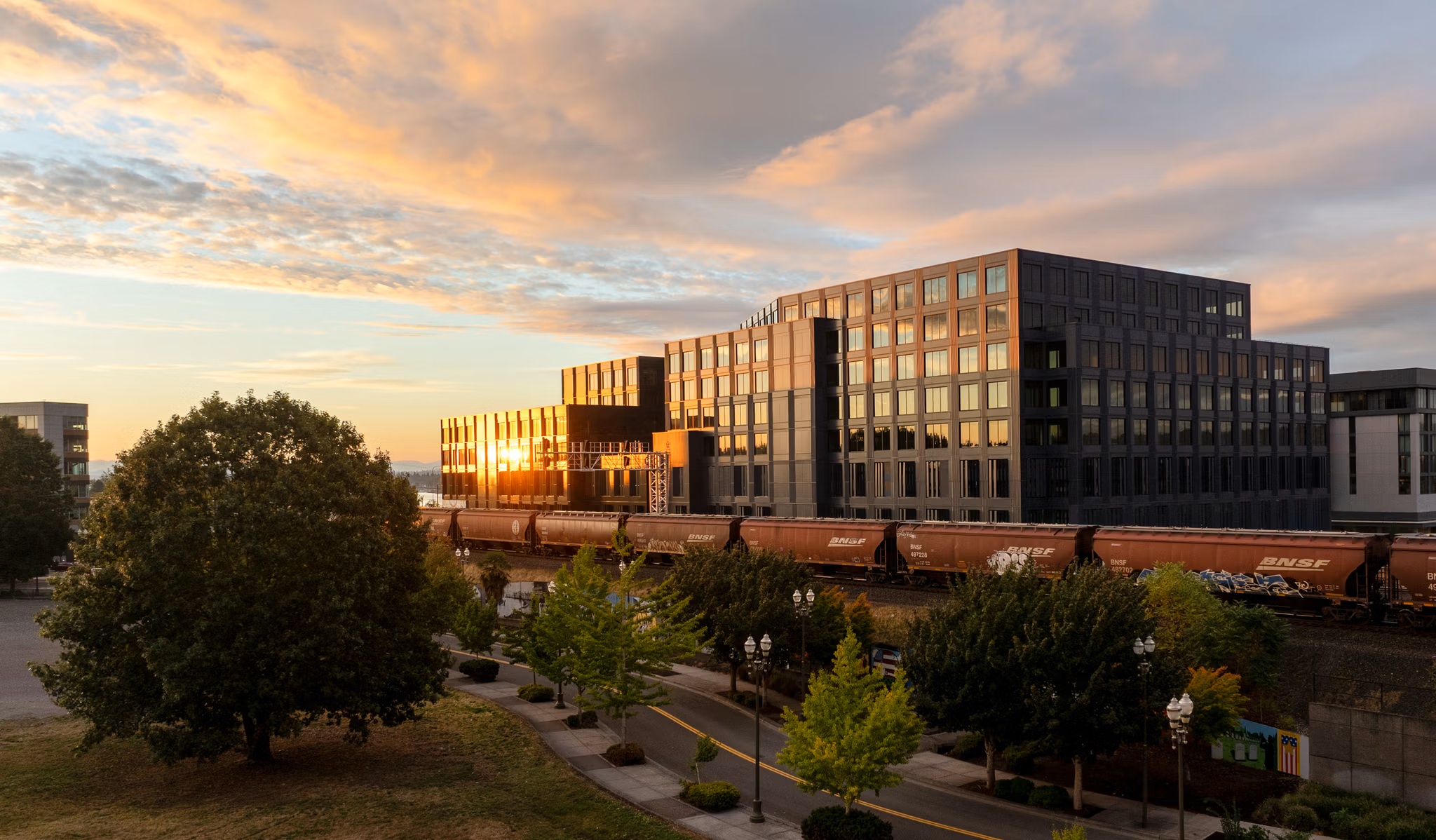 Terminal 1 at sunset behind a passing freight train, its facade catching low orange light