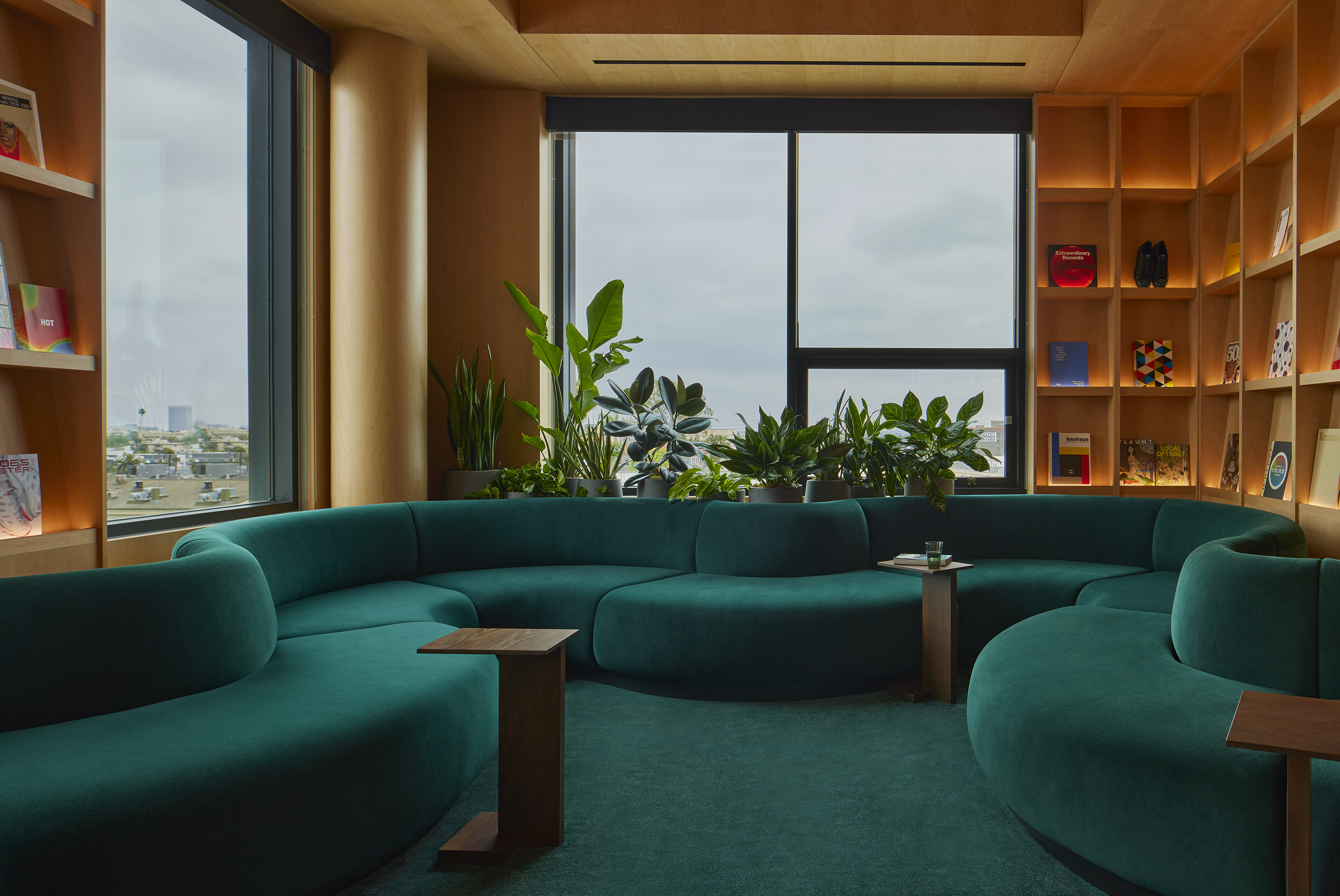Curved green velvet seating in a maple-lined library with planting at the window