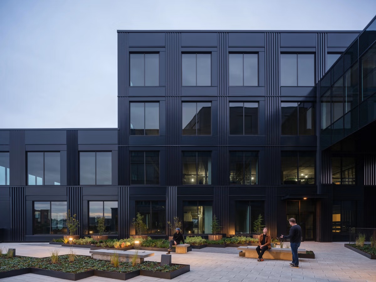 Courtyard benches and planting at dusk with people talking in front of the dark facade
